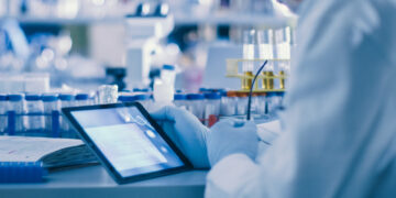 Senior Male Research Scientist is Using a Tablet Computer in a Modern High-Tech Laboratory. Genetics and Pharmaceutical Studies and Researches.